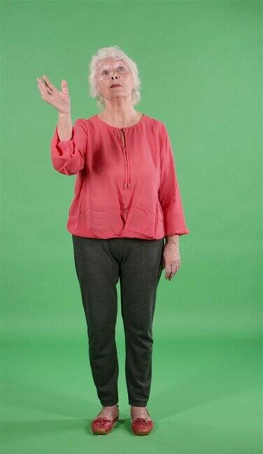 画像上的老妇人正在挥手示意过来在演播室的绿色屏幕上灰头发的祖母穿着红色衬衫缓慢的运动垂直视频