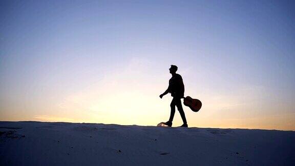 一个庄严的阿拉伯人手拿吉他走在沙漠的小山丘上在夏天的傍晚夕阳西下