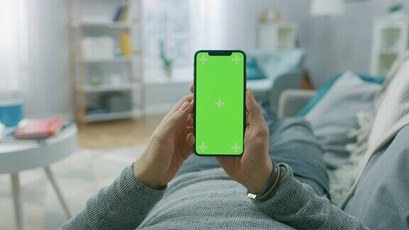 一名男子躺在沙发上使用智能手机的绿色模拟屏幕做滑动滚动手势男人使用手机互联网社交网络浏览视角相机拍摄