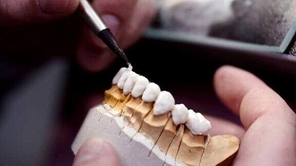 近距离观察牙科技术员绘制白色陶瓷釉在修复的工作场所的牙齿种植实验室
