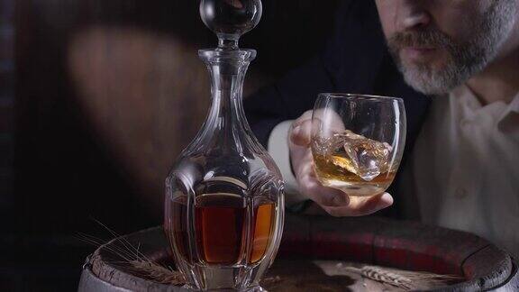 一个穿西装留着胡子的男人(侍酒师)从一个陈年威士忌酒桶里拿出一杯加冰的威士忌摇了摇酒杯让威士忌的味道散发出来慢动作4K150fps黑魔法大熊ProG2
