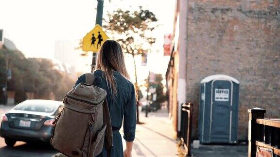 背影年轻时尚的女人与背包独自走在夏天的日落花时间在市中心