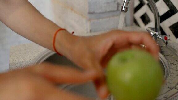 一个年轻女子正在厨房里用水龙头洗青苹果