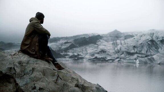 年轻英俊的男子坐在岩石上看着冰川游客独自探索冰岛的冰泻湖