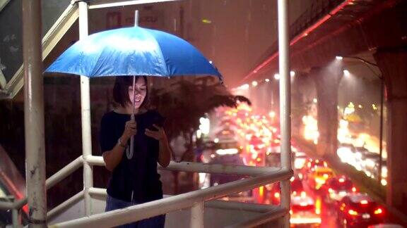 曼谷夜雨中使用智能手机的女性