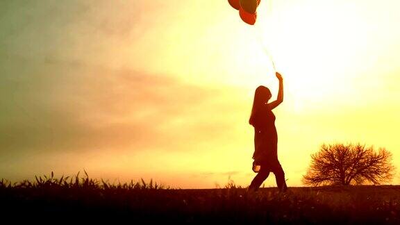 快乐的年轻女子漫步草地气球日落快乐