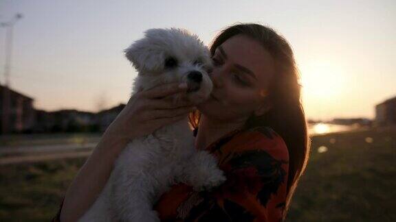 年轻美丽的女人拥抱她的马耳他狗在日落