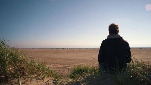 一个孤独的人坐在丹麦海滩的沙丘上看着地平线