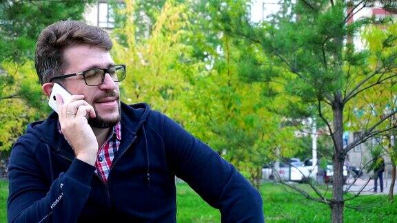 一个愉快的人坐在公园的长椅上通过电话交谈