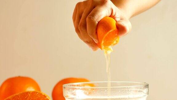 女人们用手把半个橙子挤到玻璃碗里把橙汁倒进碗里
