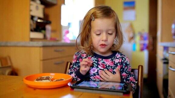 小女孩坐在餐桌前用iPad吃麦片