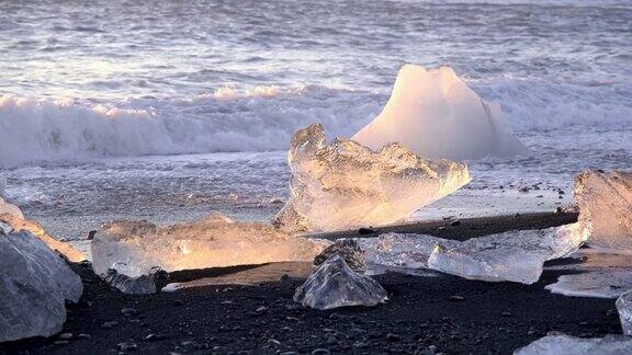 日落时冰山在黑色火山沙上闪闪发光被海浪撞击的清晰冰块冰岛著名的钻石海滩8K分辨率拍摄