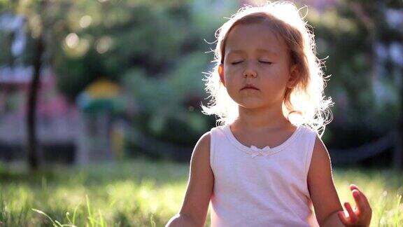 可爱的小女孩在公园的草地上做瑜伽运动