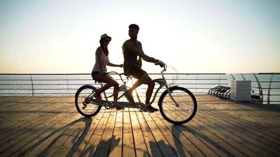 一对混合种族的夫妇在海边的户外骑双人自行车慢镜头