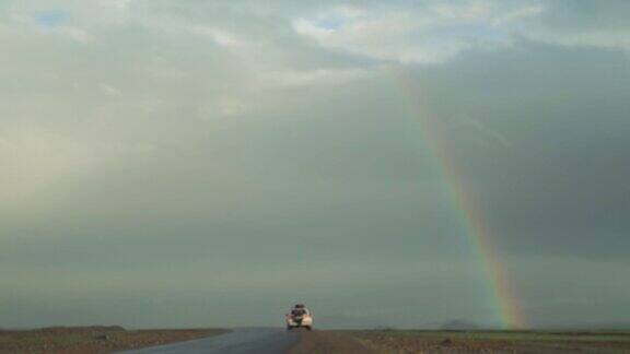 一辆白色轿车在明亮的彩虹下行驶在公路上