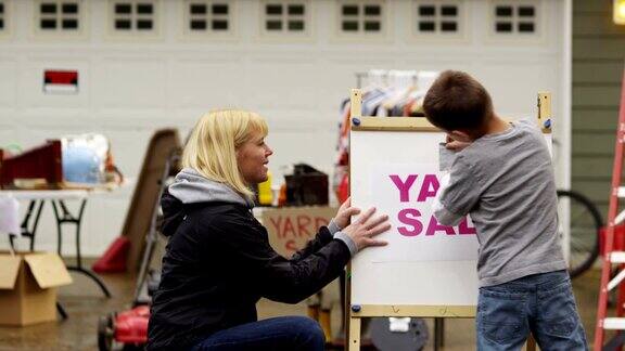 母亲在帮小男孩挂上庭院旧货出售的牌子