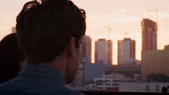 一对夫妇在屋顶露台上看日落时城市的后视图