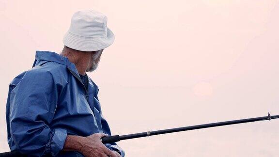 老渔夫站在海边的岩石上夕阳下垂钓