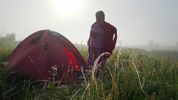 女人和登山帐篷在有雾的清晨一位老妇人在登山帐篷附近穿着夹克