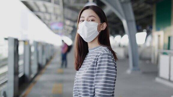 一名亚洲妇女戴着面具在站台上行走等待一辆电动火车