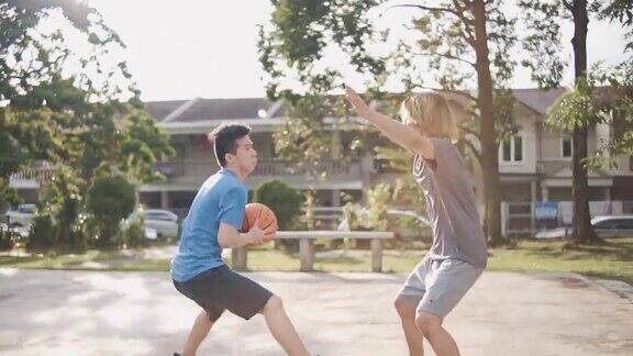 慢动作背光Z一代亚洲华人少年挑战球员和投篮在周末早上练习篮球比赛的朋友
