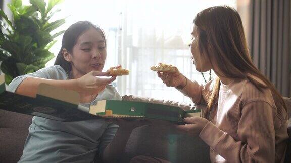两个亚洲女人朋友有乐趣分享披萨和吃披萨在家
