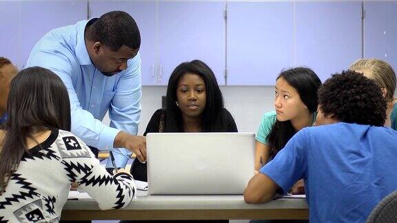 教师帮助不同种族的学生使用电脑