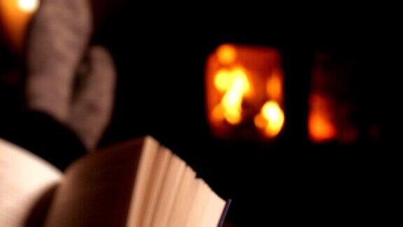 看书喝威士忌的人在燃烧木头的火炉的火焰下暖脚