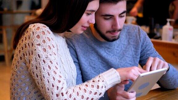 一对深情的情侣在咖啡馆看平板电脑上的照片