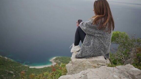 美丽的年轻女子坐在悬崖上