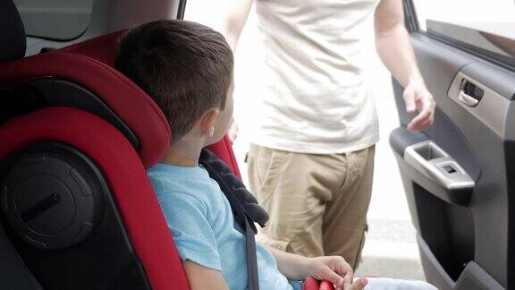 小男孩微笑着而他的父亲帮助系安全带在汽车安全座椅