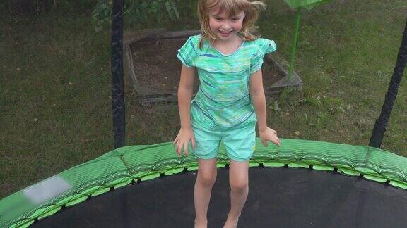 快乐的女孩穿着绿松石t恤在蹦床上跳得很开心