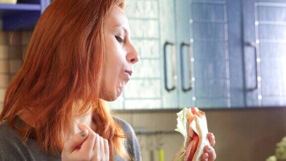 迷人的年轻红发女孩在周末的清晨在厨房吃俱乐部三明治吃不健康食品汉堡享受晚餐的女人在舒适的厨房里吃早餐