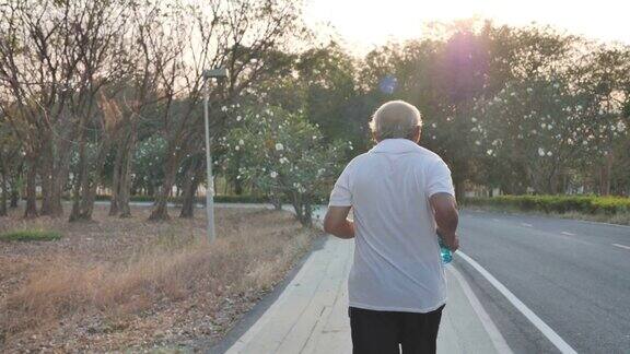 后视图亚洲老年人锻炼一位老人在傍晚有阳光的公园里的道路上跑步健康的生活方式和锻炼慢动作