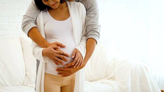 幸福的孕妇和她的丈夫抱着和听婴儿在肚子里