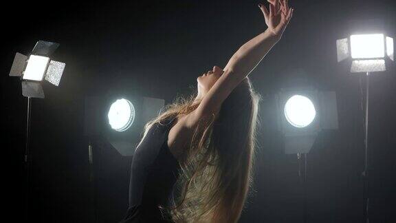 职业芭蕾舞演员在聚光灯下跳芭蕾舞大舞台上烟雾缭绕美丽的白人年轻女孩与长发穿着黑色紧身衣泛光灯背景慢动作