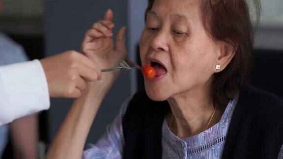 年轻的亚洲妇女给祖母喂食物