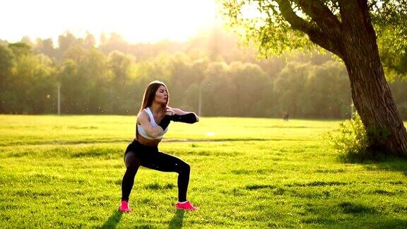 年轻的健身女性在公园中做深蹲锻炼