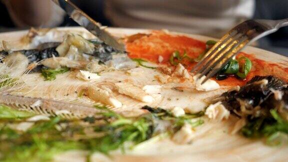 一个女人在咖啡馆用刀叉吃剩菜鱼
