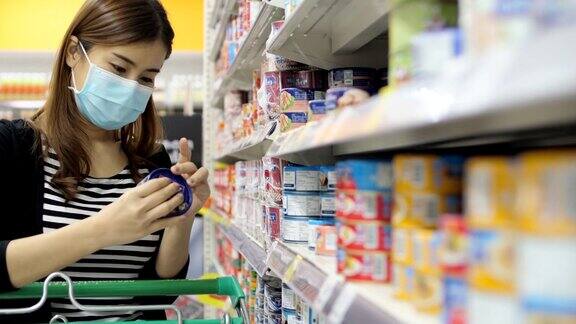 年轻的亚洲妇女带着防护口罩在超市购物阅读清单