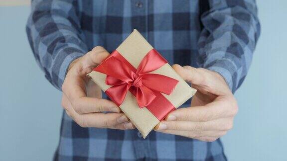 用手工纸包着的小礼盒手里系着红色的蝴蝶结情人节的礼物在男人手中男人拿着一个带红丝带的盒子在展示节日