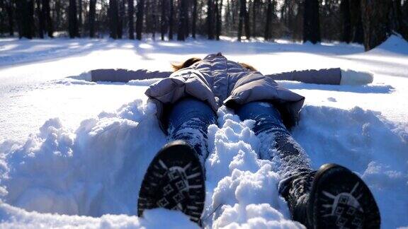 穿着冬衣的少女躺在白雪覆盖的草地上像天使一样快乐的女人在雪地里玩享受冬天的时光快乐的女士在户外玩寒假慢镜头