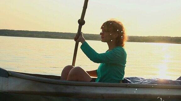 日落时分年轻的红发女孩划着皮划艇运动旅游