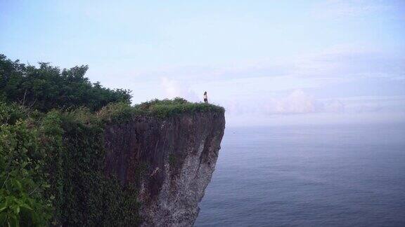 一个女人站在悬崖上看着巴厘岛乌鲁瓦图的海边