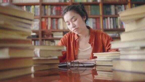 心烦意乱的亚洲女学生坐在书堆后面学业压力