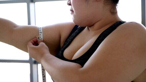 不快乐的超重妇女穿着运动服用卷尺测量手臂