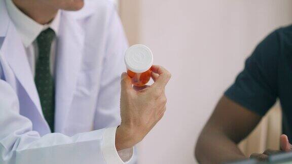 亚洲男性医生手里拿着药瓶向他的病人解释