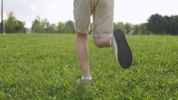 一个男孩的腿在绿色的草地上跑步的慢镜头