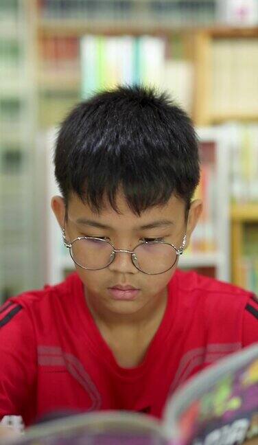 一个戴眼镜的青少年在公共图书馆看书的特写镜头