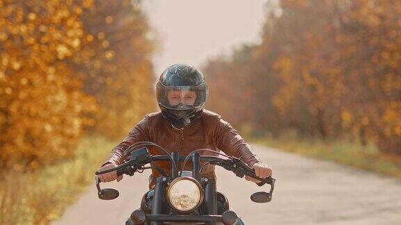 一个戴着头盔的年轻人在秋天的路上骑着摩托车骑摩托车的人在高速公路上快速行驶肖像的观点